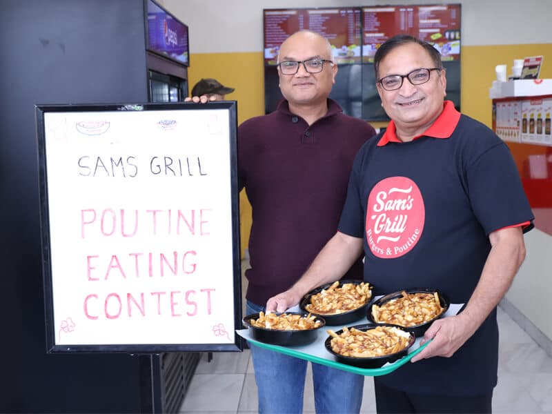 A tray of four contest poutines held up beside the hand-lettered contest sign: fresh-cut fries, real curds, vegetarian gravy.