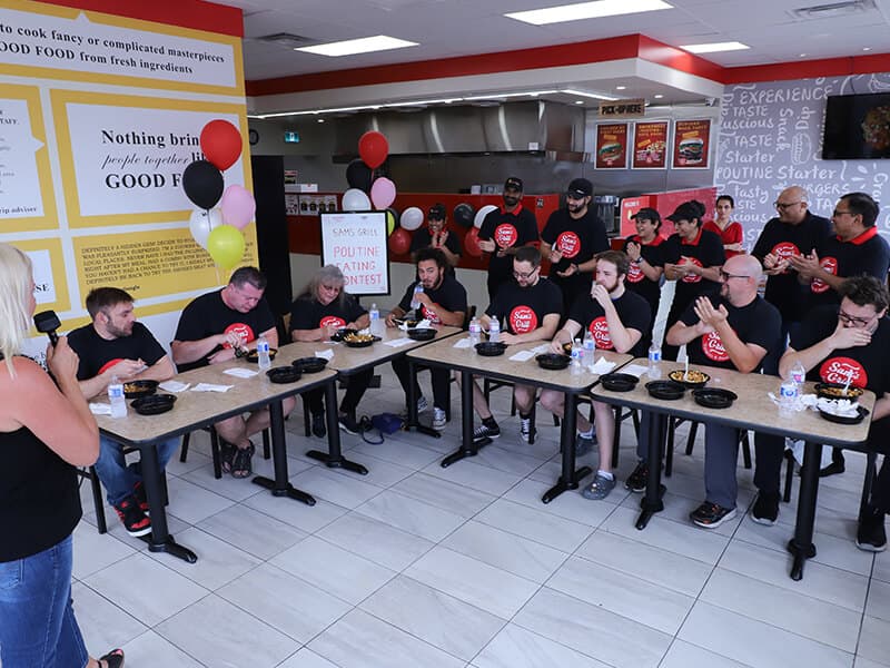 The whole room on its feet around the tables while the contestants eat, staff clapping them through it.
