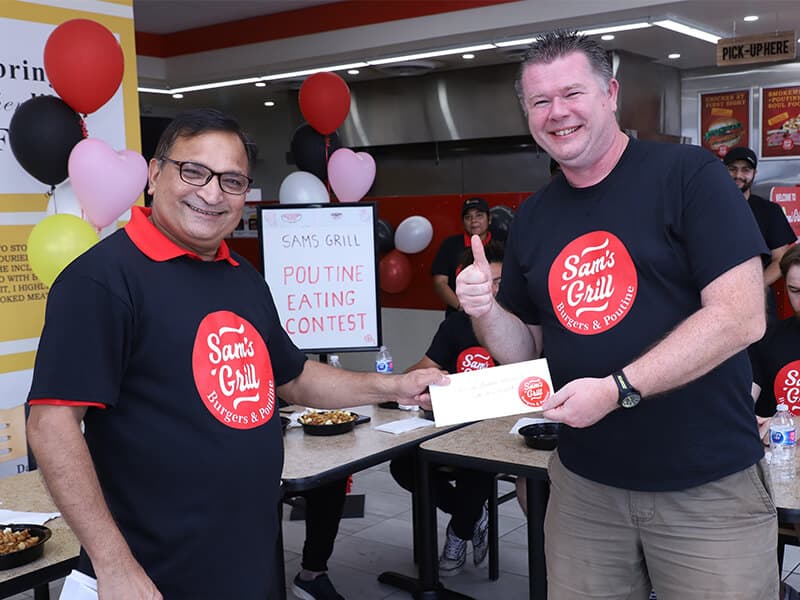 The winner shaking hands for the envelope, thumbs up, contest sign still on the table behind.